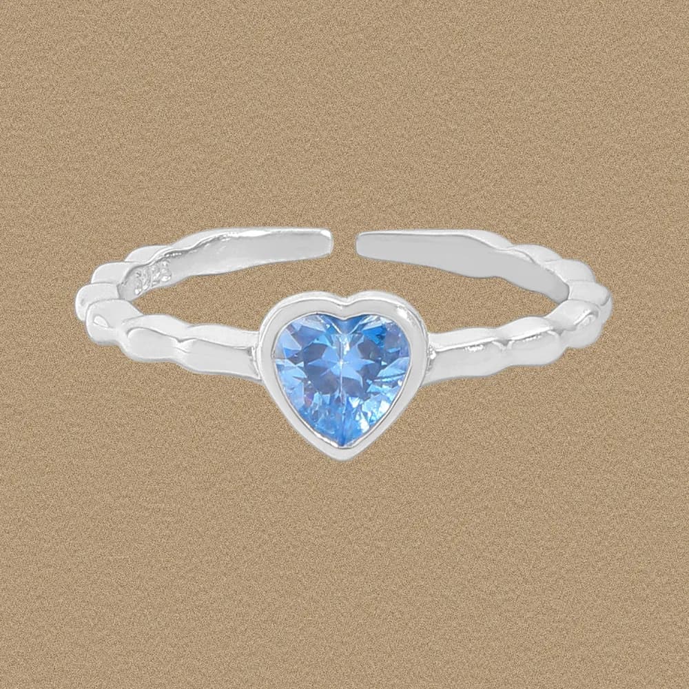 Close-up of a sterling silver ring with a heart-shaped blue gemstone set in a bezel on a warm background.