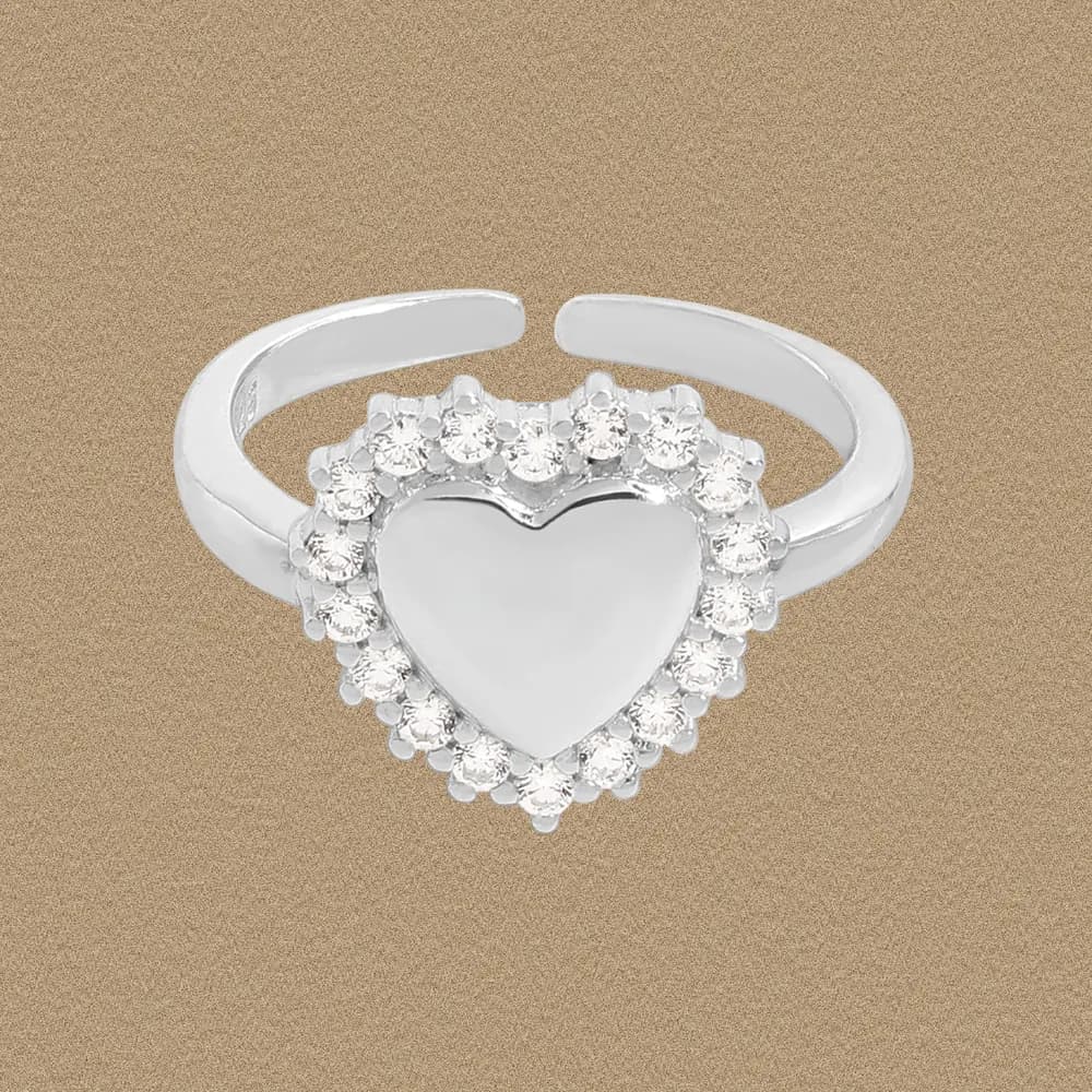 Polished sterling silver ring with a heart-shaped center and crystal halo on a beige background.