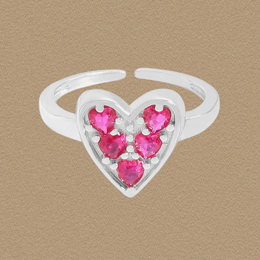 Silver ring with a heart-shaped face set with four pink stones on a neutral background.