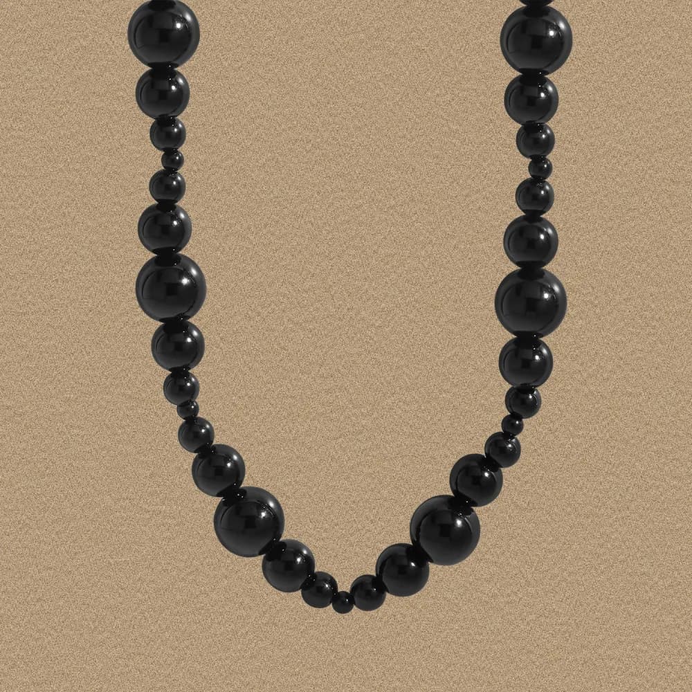 Close-up of a polished black bead necklace against a warm beige background.