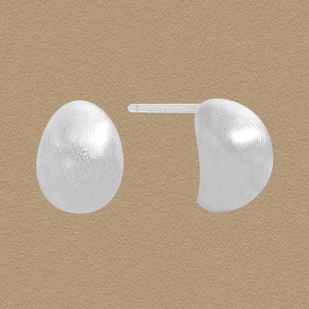 Close-up of oval sterling silver stud earrings with a subtle textured surface and posts visible