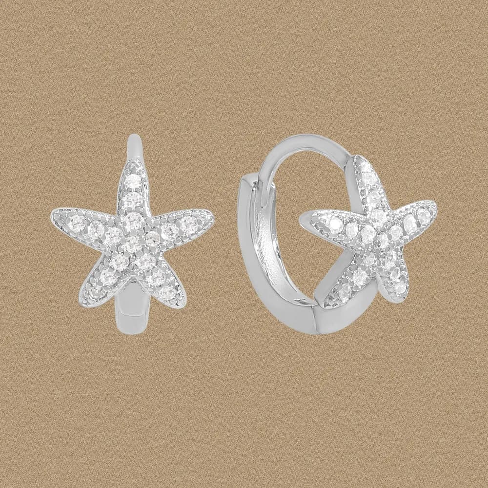 Front view of sterling silver starfish pavé hoop earrings against a sandy background.