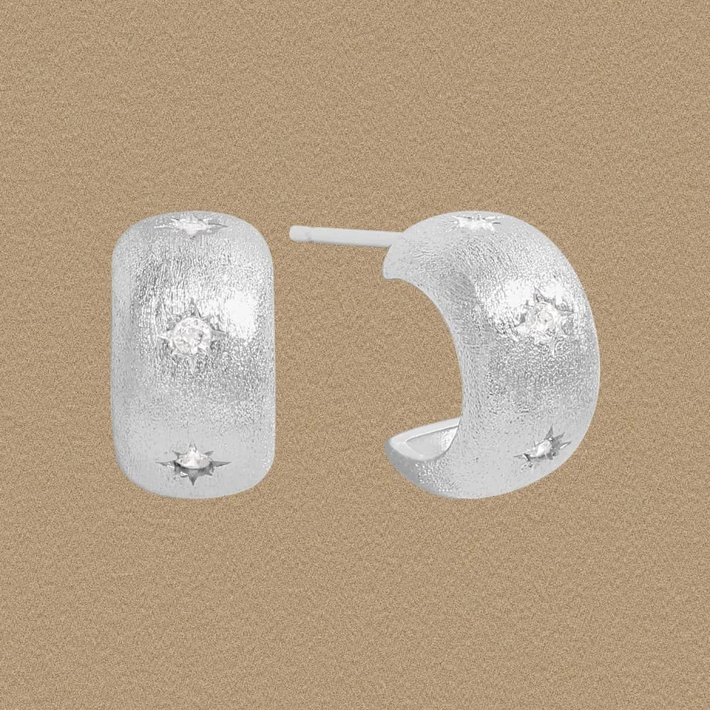 Textured sterling silver hoop earrings with small starburst accents on a rounded rectangular surface.