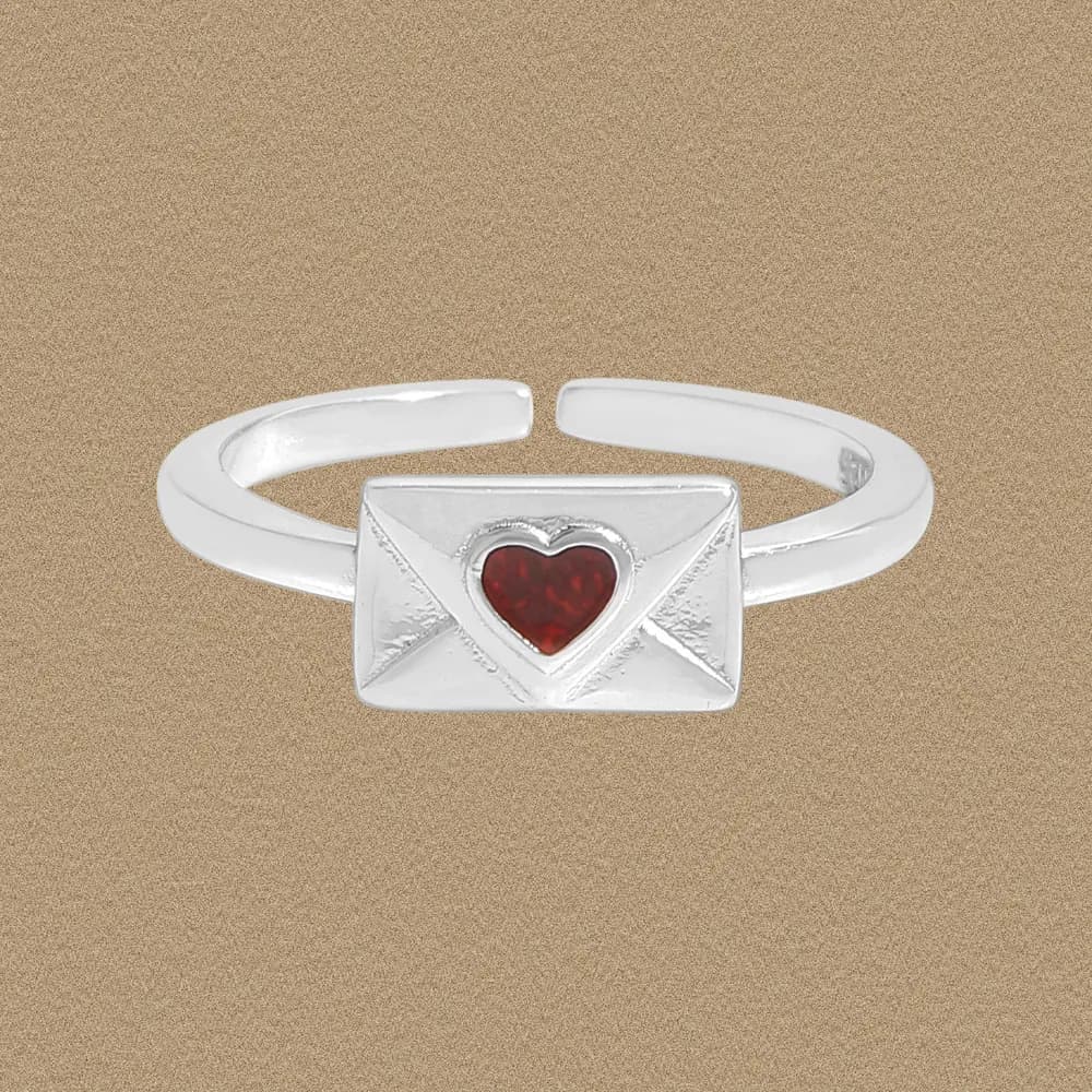 Polished sterling silver ring with a rectangular envelope motif and heart-shaped red stone on an beige background.