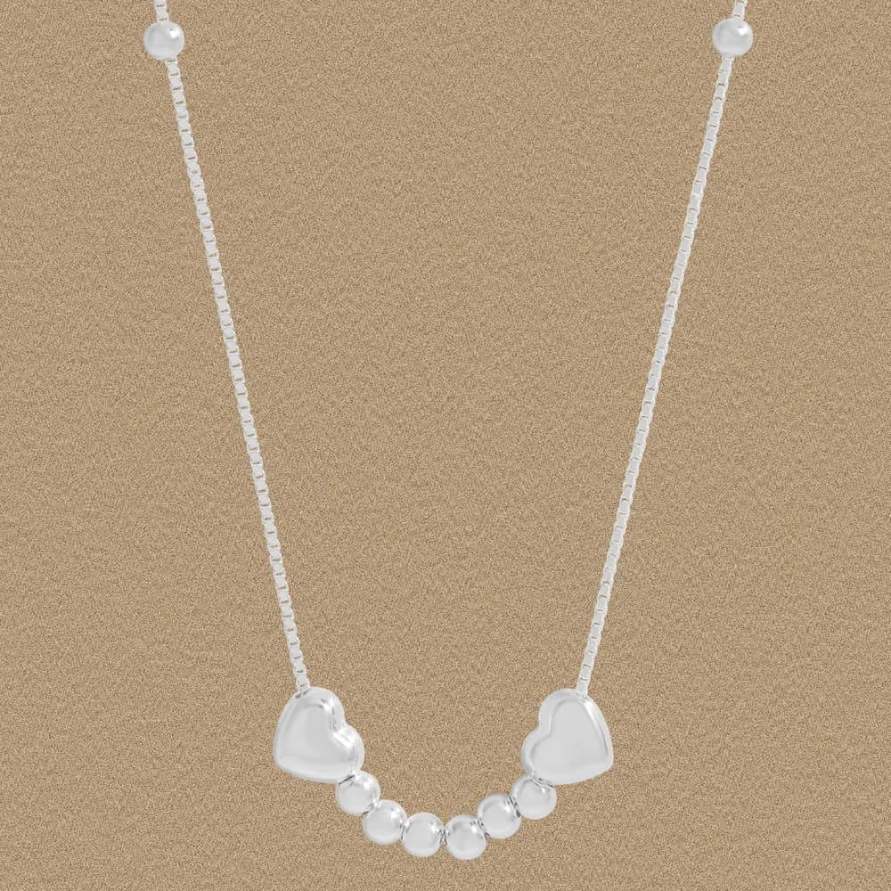 Polished sterling silver necklace with two heart pendants and a row of beads hanging between them.