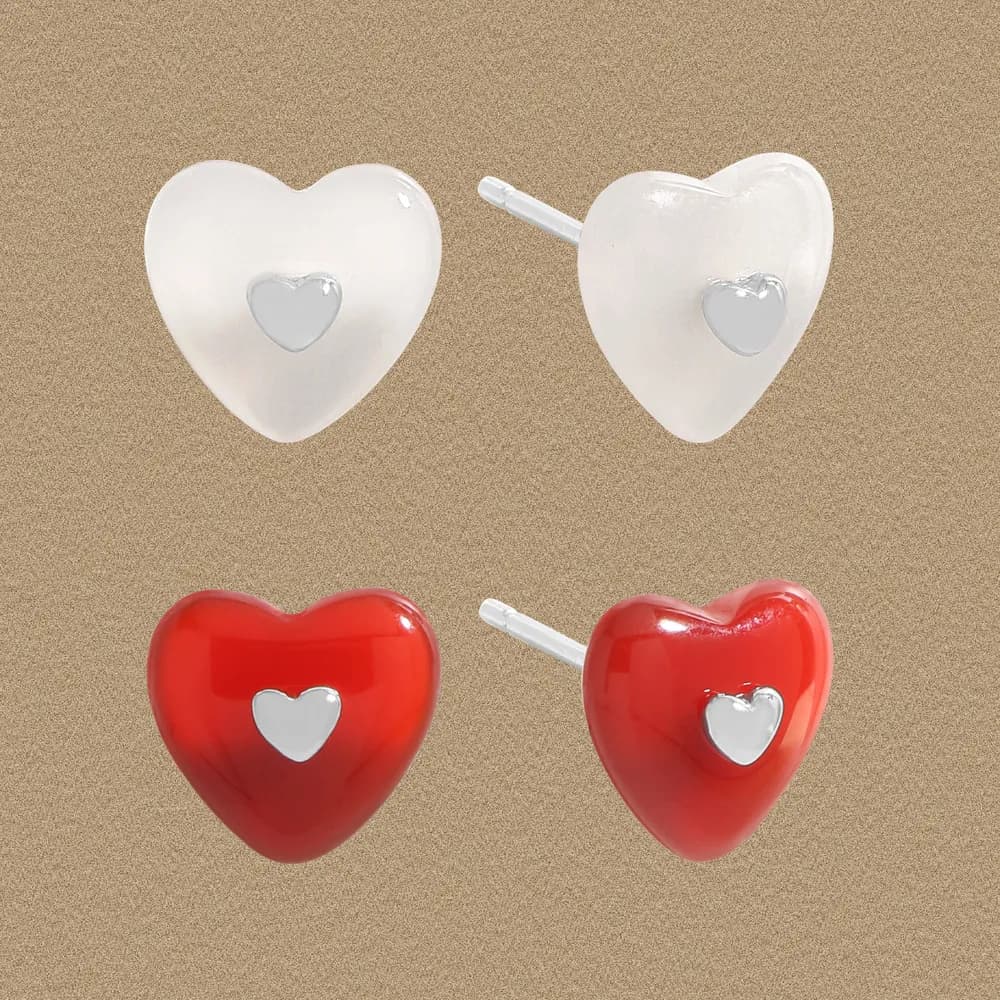 Pair of heart-shaped stud earrings in white and red enamel with silver inner hearts on a caramel background.