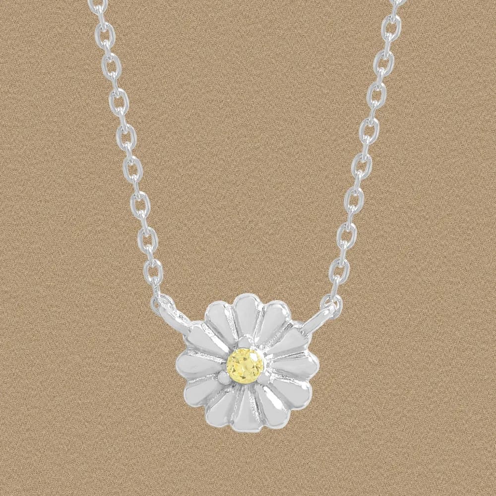 Sterling silver daisy pendant on a delicate chain against a warm beige background.