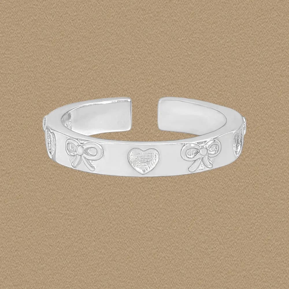 Polished sterling silver open-band ring with heart and bow motif against a warm tan background.