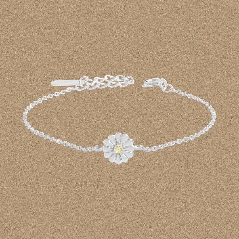 Polished sterling silver daisy bracelet with a yellow center stone resting on a sandy background.