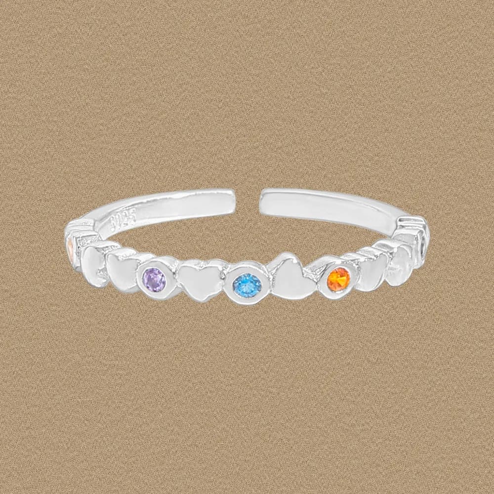 Polished sterling silver ring with heart motifs and colored gemstone accents on a beige background.