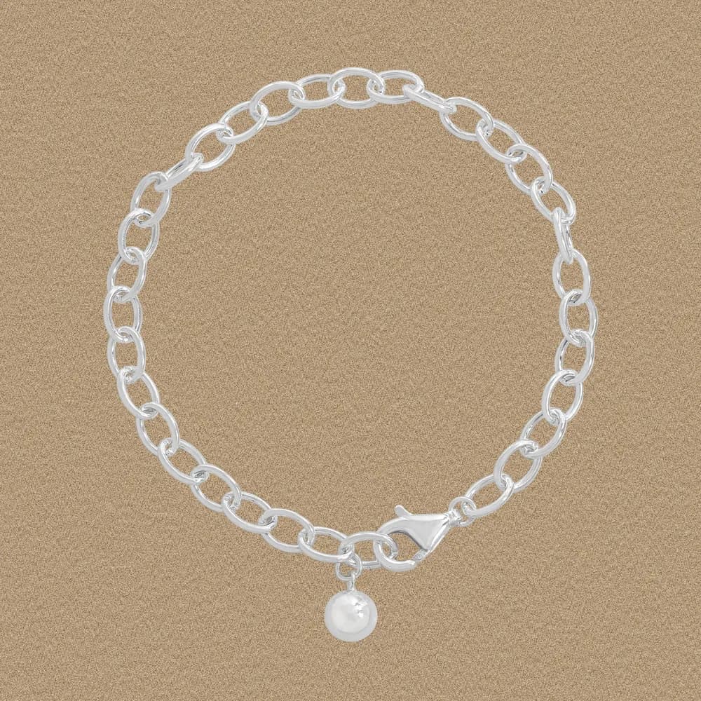 Polished sterling silver chain bracelet with a pearl charm resting on a sandy surface.