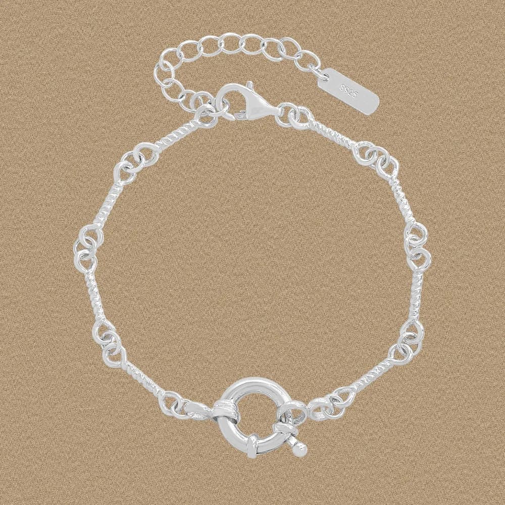Polished sterling silver bracelet with a circular toggle clasp and mixed-texture chain on a warm background.
