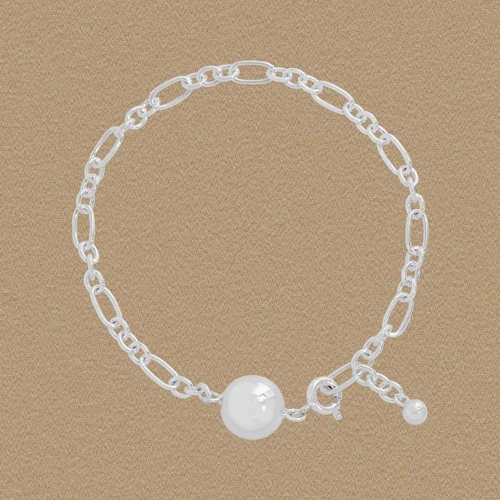 Sterling silver chain bracelet with a large central pearl bead and a small pearl charm on a sandy background.