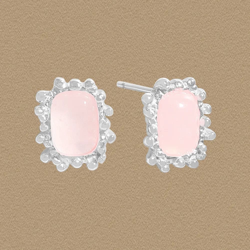 Close-up of pink rectangular cabochon halo earrings with a beaded silver surround on a beige background.
