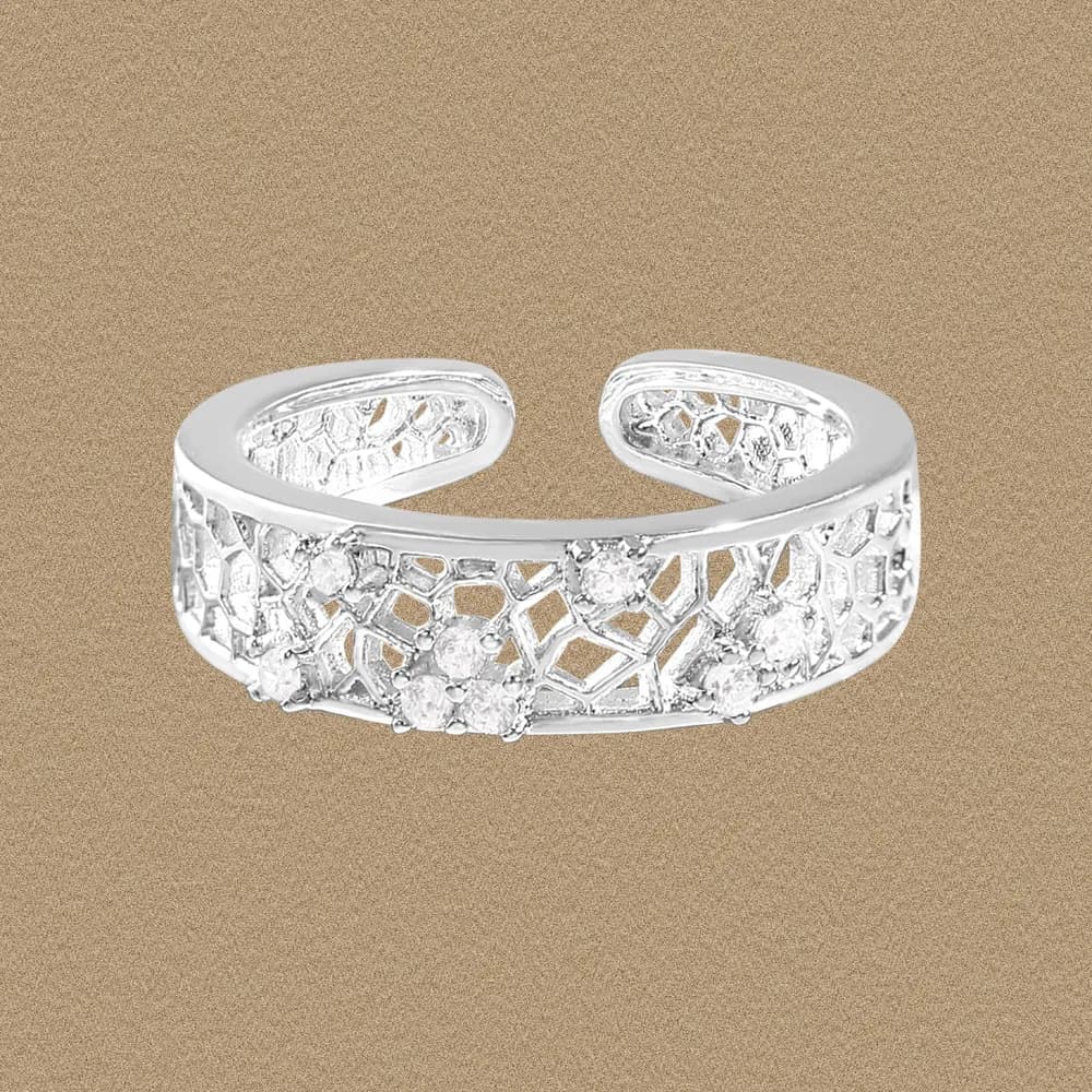 Polished sterling silver openwork ring with floral lattice and stones on a warm beige background.