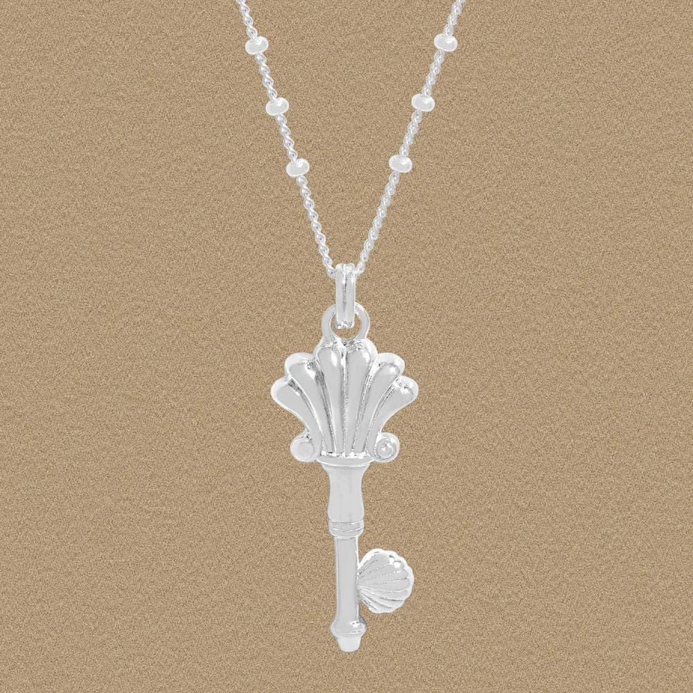Polished sterling silver shell-key pendant on a beaded rolo chain against a warm background.