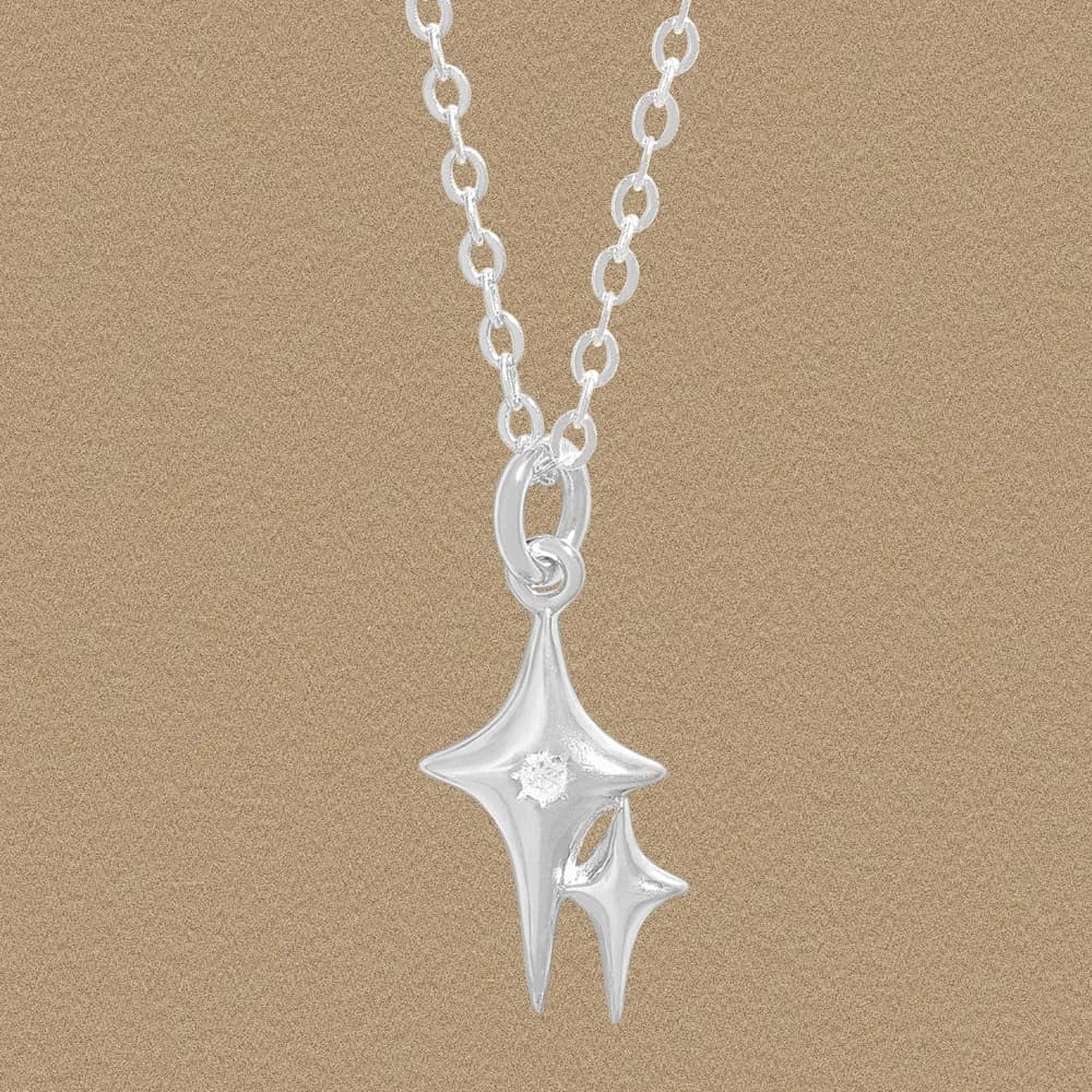 Polished sterling silver starburst pendant on a chain against a beige background.