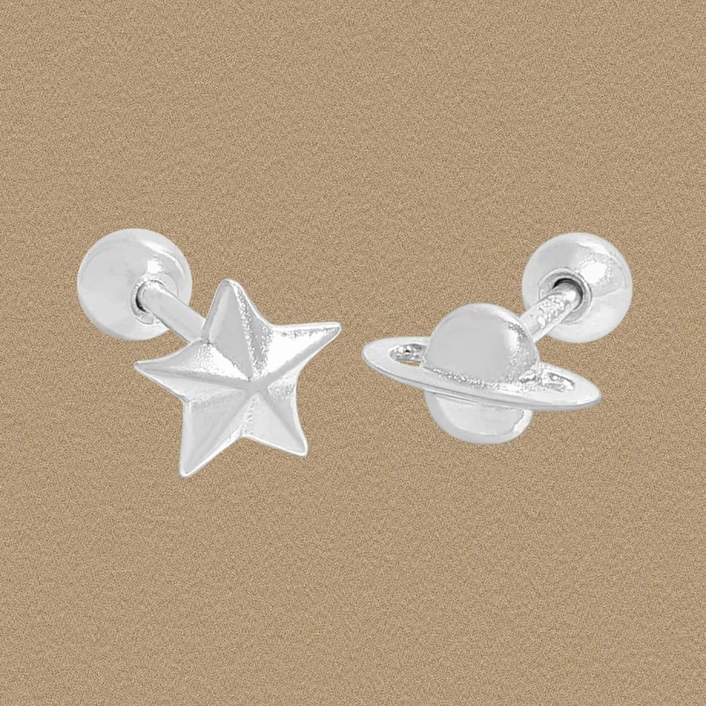 Sterling silver star and planet stud earrings on a warm beige background.