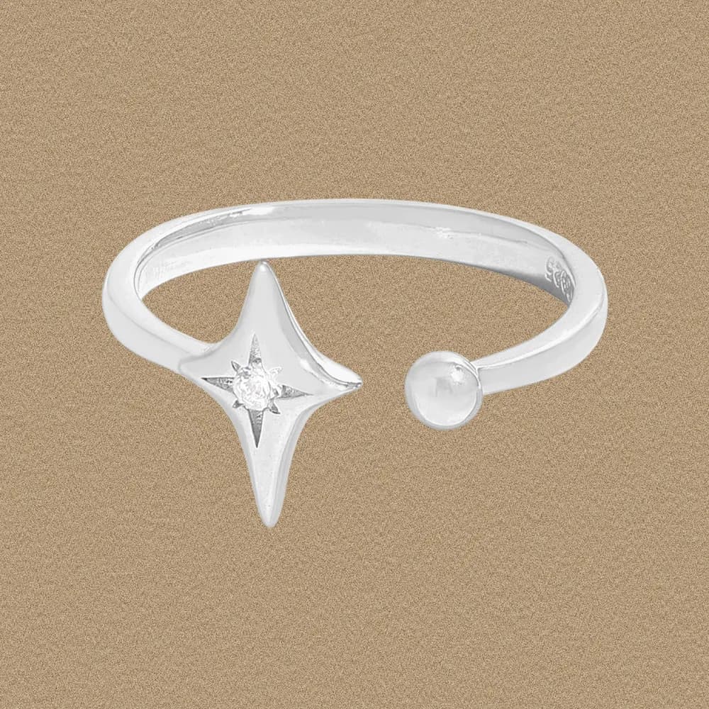 Polished sterling silver open ring with a starburst motif and bead on a light brown background.