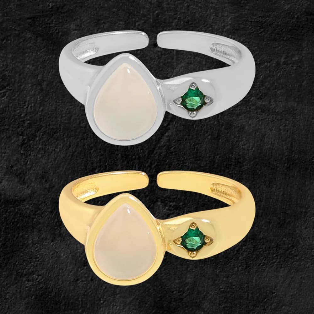 Open-band ring in silver and gold-tone finishes with a milky teardrop centerpiece and a small green gemstone on the side.